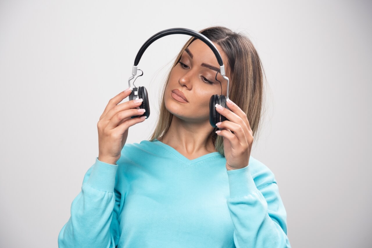 Uma jovem observa admirada seu headfone com áudio HD.